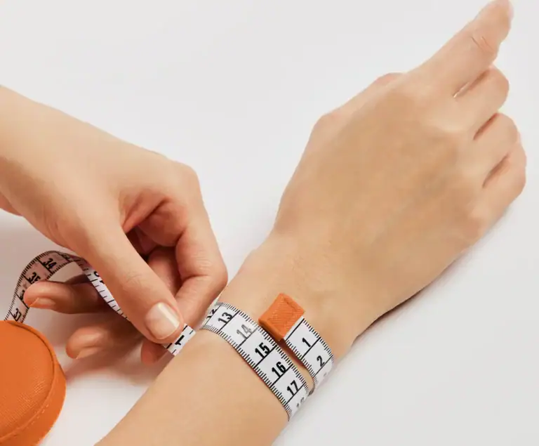 A tape measure being wrapped around a wrist, just below the wrist bone
