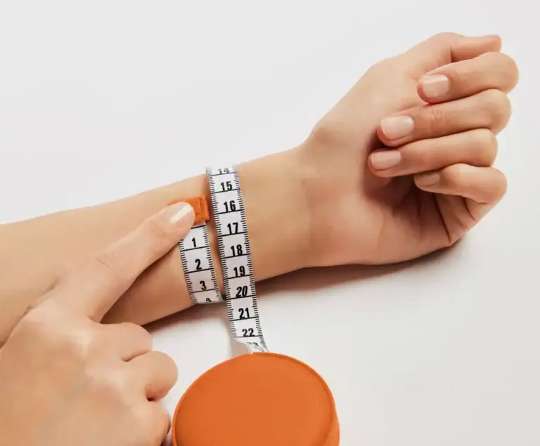 A fingertip marking the point where the tape measure meets around the wrist