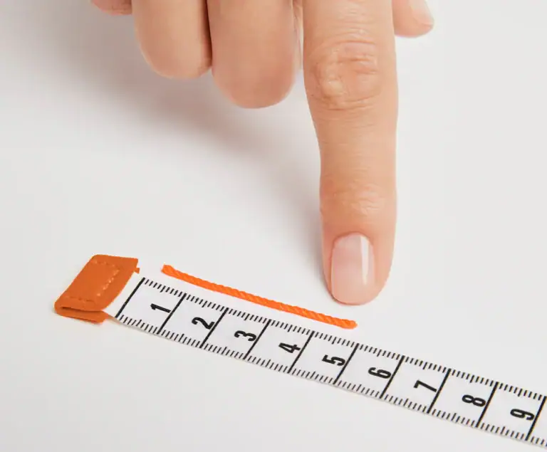 A cut length of string laid against a tape measure to read the finger circumference